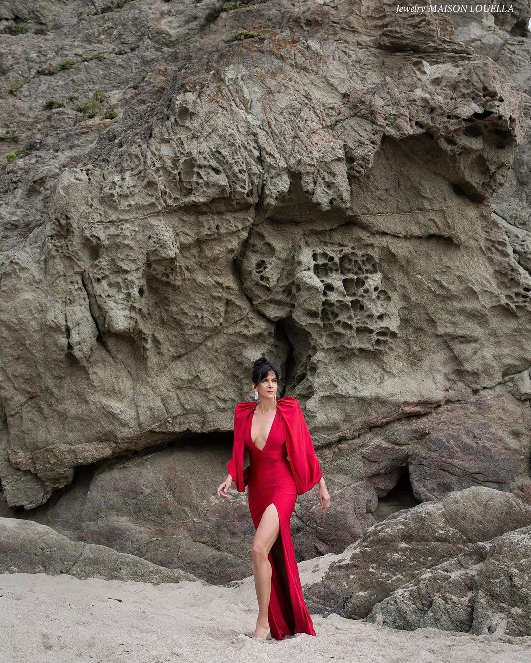 Actress Patricia Velásquez in a red gown with a draped cape and high slit against a Malibu rock face for BLOWE Magazine, styled by Quentin Fears